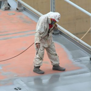 worker painting ship hull using airbrush gray paint
